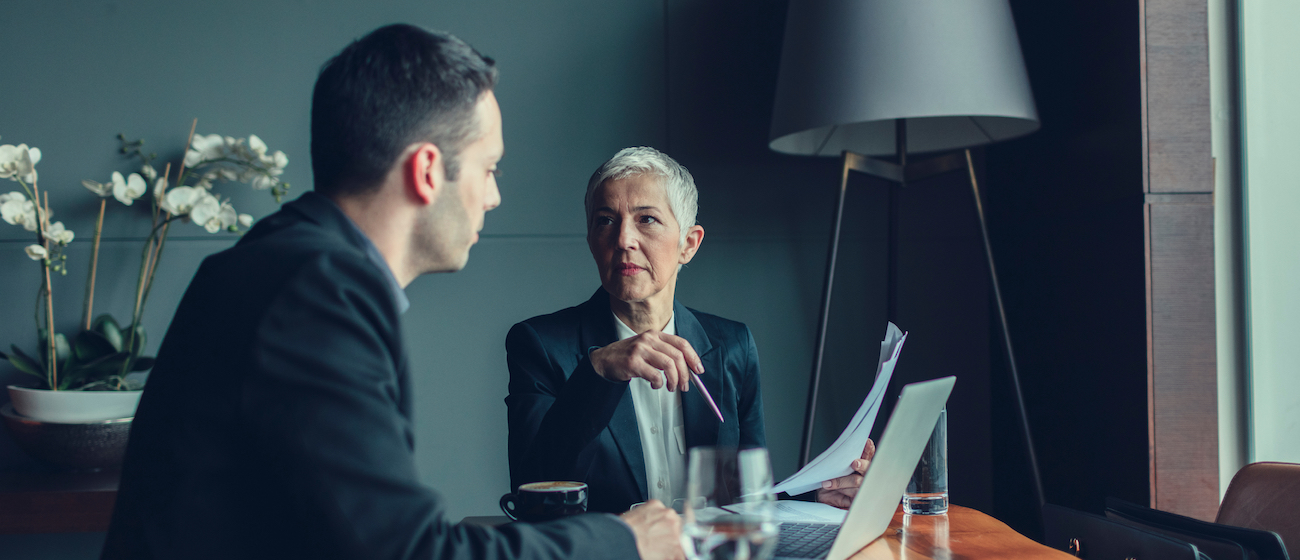 Mature businesswoman, CEO, have meeting with her coworker. Businessman talking with his female manager, mature businesswoman. In front of them, on the table, is laptop. They are focused on their work.