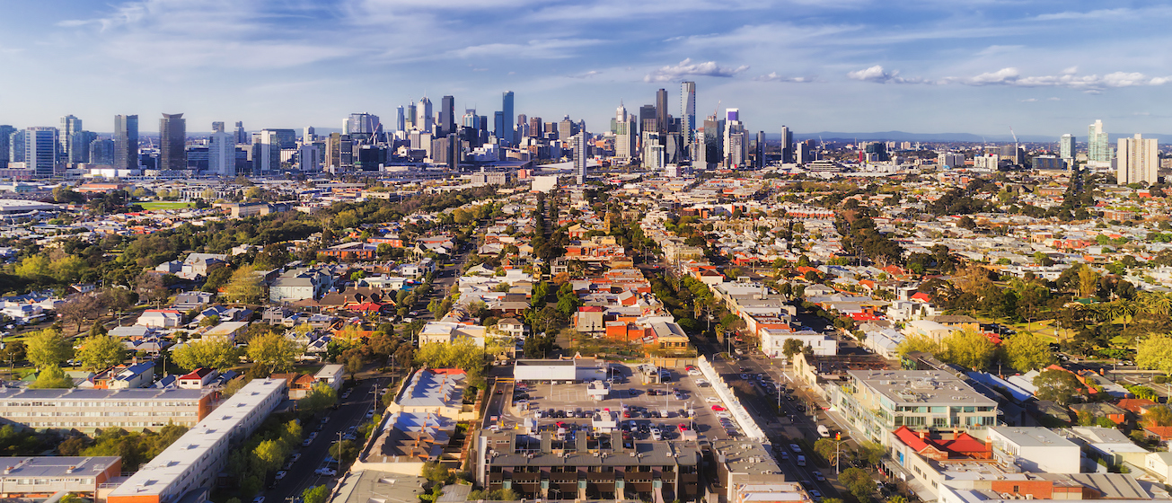 Aerial view of Melbourne city CBD high-rise towers from Port Melbourne and Southbank above residential suburb house roofs and local streets, roads, cars and parks.