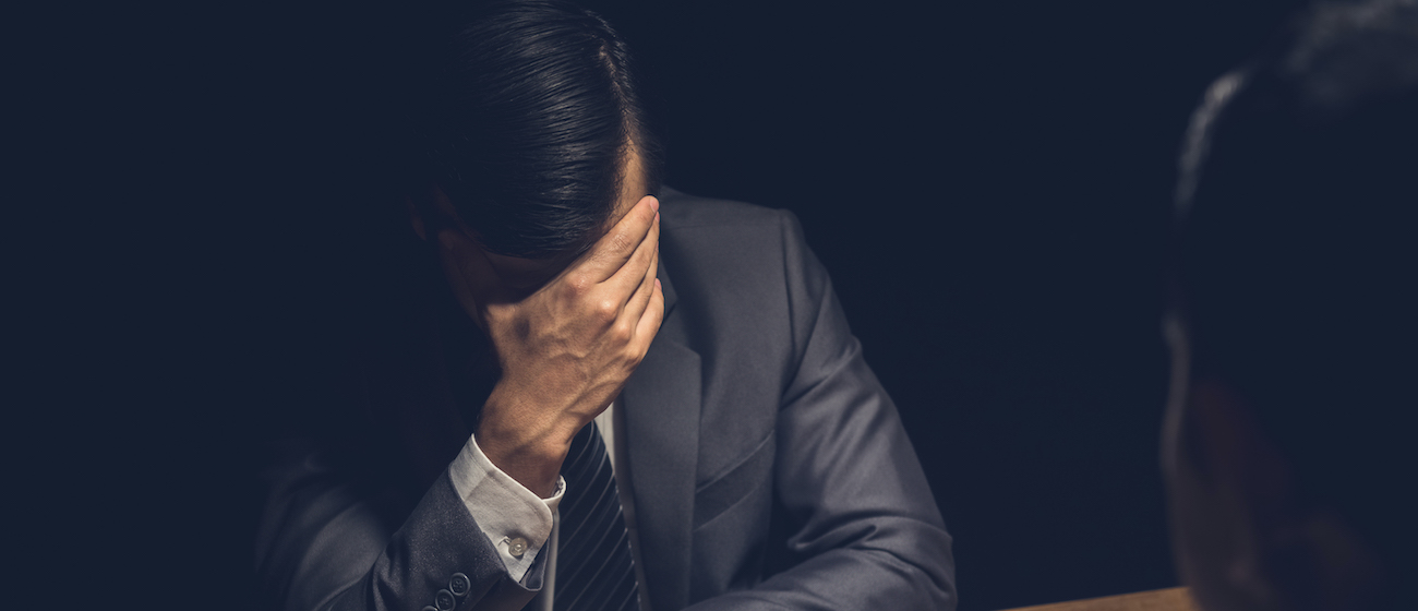 man displaying regret, worry and concern using body language in dark interrogation room