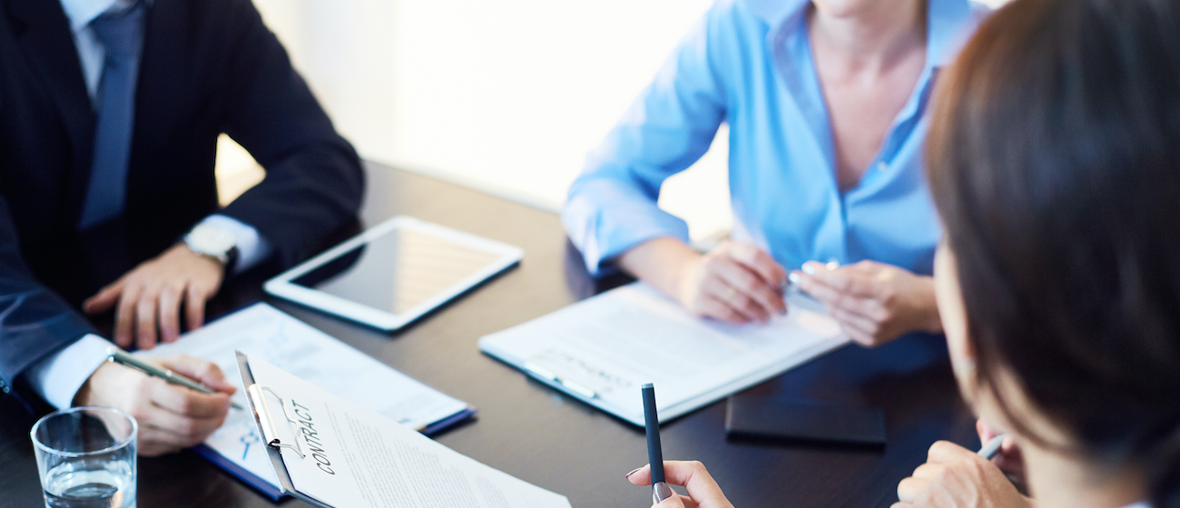 Unrecognizable business partners discussing agreement conditions reviewing it together at meeting